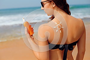 Skin care.Sun protection. Beautiful woman in bikini apply sun cream on Face. Woman with Suntan lotion on beach.