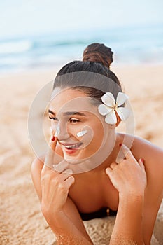 Skin care. Sun protection. Beautiful Woman In Bikini apply sun cream on Face. Woman With Suntan Lotion On Beach. Portrait Of Femal