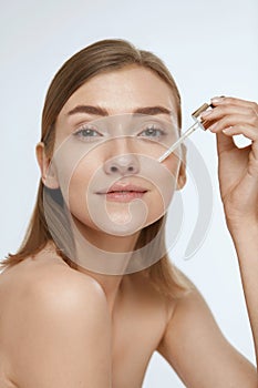 Skin care. Woman applying serum or facial oil on beauty face