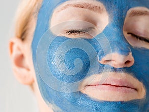 Skin care. Woman face with blue clay mud mask close up. Girl taking care of oily complexion. Beauty treatment.