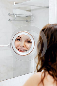 Skin care. Woman touching hair and smiling while looking in the mirror.Portrait of happy girl with wet hair in bathroom