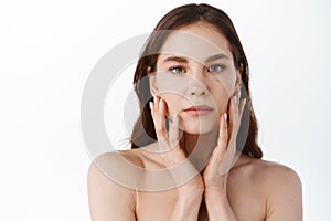 Skin care. Young beauty woman with natural make up, touching hydrated and nourished facial skin, holding hands on cheeks
