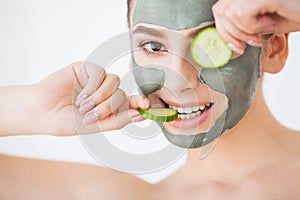 Skin Care. Young woman with cosmetic clay mask holding cucumber