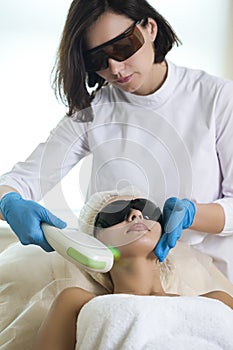 Skin Cosmetology Concepts. Close-up of Young Winsome Woman in UV Protective Glasses During Laser Skin care on Face Using