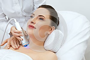 Skin Cosmetology. Woman Doing Blue Light Therapy On Neck