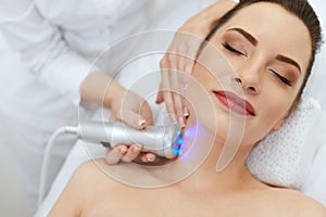 Skin Cosmetology. Woman Doing Blue Light Therapy On Neck