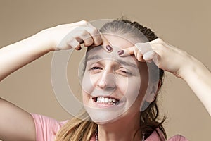 Skin and Healthcare Issues. Portrait of Young Caucasian Blond Woman With Skin Problems Squeezing Pustules By Fingers Against Beige