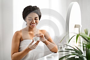 Skin Nourishing. Beautiful Smiling Black Woman Opening Jar With Face Cream