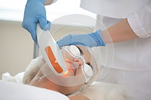 Skin Procedures. Female Woman Receiving Facial Beauty Treatment While Removing Pigmentation in Clinic During Pulsed Laser Light