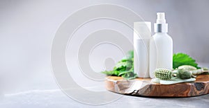 Skincare beauty routine at home bathroom. Face jade roller massager, nettle lotion, cream, shampoo in white bottles and nettles