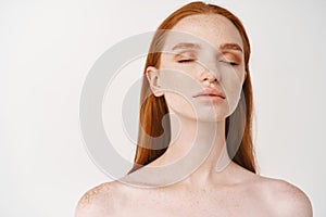 Skincare and beauty. Young sensual redhead woman standing naked with closed eyes, showing perfect, healthy skin on face