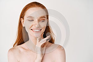 Skincare. Close-up of redhead woman with pale soft skin, smiling white teeth and touching clean no makeup face, looking