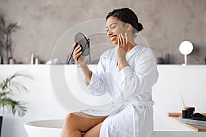 Skincare Concept. Beautiful Black Woman Looking In Magnifying Mirror And Touching Face