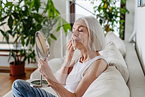 Skincare for mature woman. Portrait of beautiful older woman with gray hair cleaning, taking care of her skin.