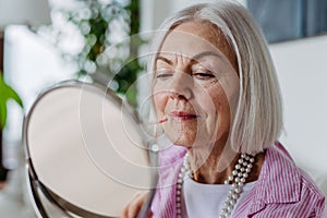 Skincare for mature woman. Portrait of beautiful older woman with gray hair putting makeup on.