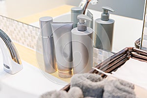 Skincare products including toner, face wash, and pump liquid in grey bottles at bathroom sink, showing hand towels and paper