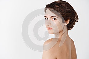 Skincare. Rear view of young caucasian woman turn head back at camera, standing half naked on white background and