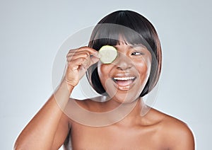 Skincare, smile and happy black woman with cucumber In studio for wellness, shine or dermatology on grey background