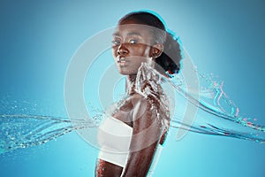 Skincare, water and black woman with a splash for hydration, cleaning and beauty against a blue studio background. Spa