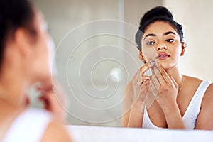 Skincare, woman and mirror to pop pimple on face with hands, dirt or scar on skin in home. Dermatology, facial wellness