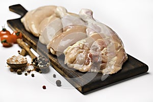 Skinless raw chicken thighs with ingredients for cooking on a wooden cutting board on white background