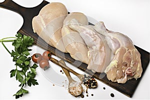 Skinless raw chicken thighs with ingredients for cooking on a wooden cutting board on white background