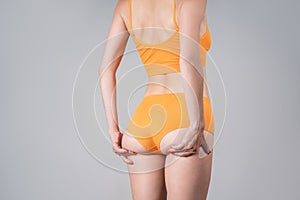 Skinny female buttocks in yellow panties on gray background, anti cellulite massage