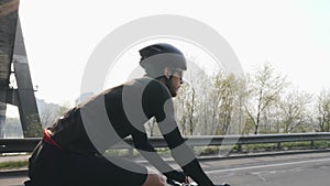 Skinny fit cyclist riding a bicycle under the bridge. Back side follow shot of bike rider pedaling bicycle on the road.