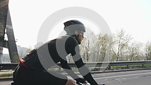 Skinny fit cyclist riding a bicycle under the bridge. Back side follow shot of bike rider pedaling bicycle on the road. Slow motio