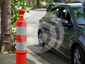 Skinny orange safety cone on sidewalk near street parking cars