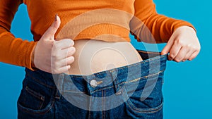 Skinny weight loss woman show flat stomach pulling oversized big blue pants jeans showing thumbs up sign. Slim body low