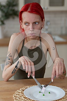 Skinny woman holding knife and fork sitting near empty plate