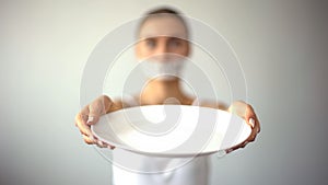 Skinny woman with taped mouth showing empty plate, concept of fasting, hunger