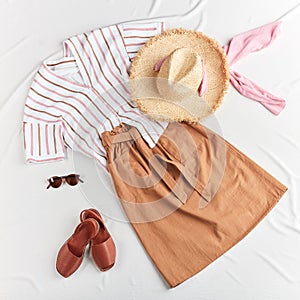 Skirt, shirt, straw boater hat, leather brown sandals on white background.