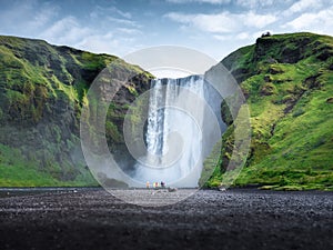 Skogafoss waterfall, Iceland. Mountain valley and clear sky. Natural landscape in summer season. Icelandic nature. Group of a peop