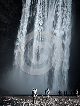 Skogafoss waterfall with tourists taking photos under the stream