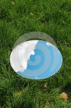 sky and cloud reflection in round mirror on grass