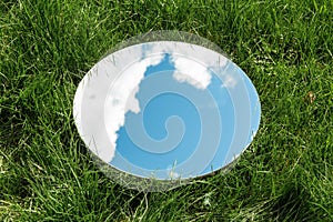 sky and cloud reflection in round mirror on grass