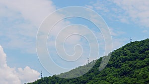 Sky cloud timelapse in background of high voltage tower on green mountain