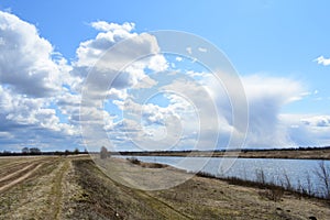 Sky, clouds. Rural road. River. Boundless field. Forest in the distance. Rural view of nature