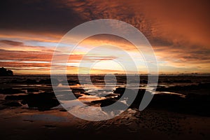 Sky with deep hanging storm clouds and wet sludge during low tide swathed in yellow and red bright light during sunset photo