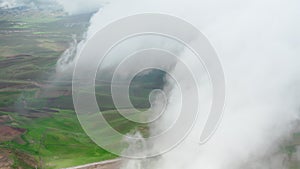 A sky shot shot through rain clouds with a view of green and brown earth fields. A bird's-eye view above the clouds with