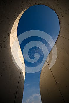 Sky shown through a curvy concrete structure .