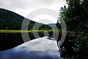 Sky and tree reflecting in almost black Lispach lake near La Bresse