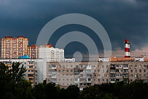 The sky is very dark blue over multi-storey buildings before a thunderstorm, with pipes visible on the horizon