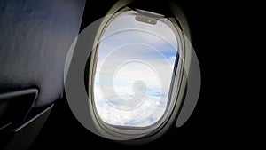 Sky view with white clouds from window of passenger seat in cabin on commercial airplane. Transportation and travel concept.