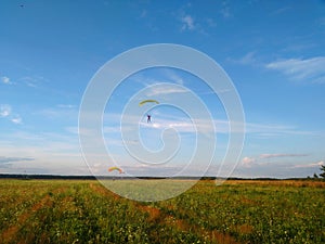 A skydiver with a bright multicolored parachute flies against the background of a blue sky