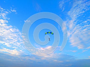 A skydiver with a bright multicolored parachute flies against the background of a blue sky