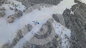 Skydiver flies over mountains covered with snow and ski lift.