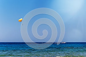 Skydiver flying with a yellow parachute by speed boat on sea. Skydiver control parachute down on surface of the sea